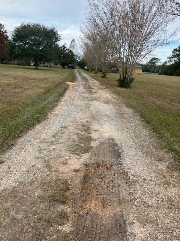 Before gravel refresh on a long rural driveway with worn dirt tracks.