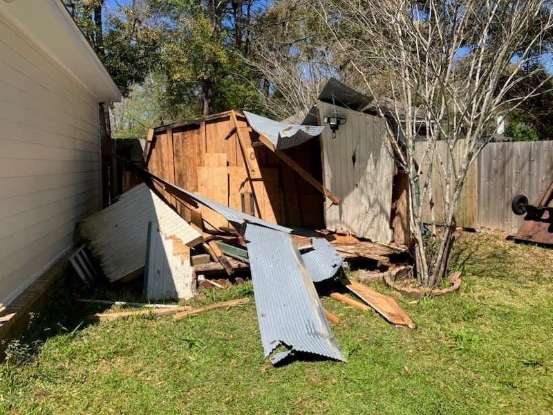 Before junk removal with collapsed shed debris piled near a fence line.